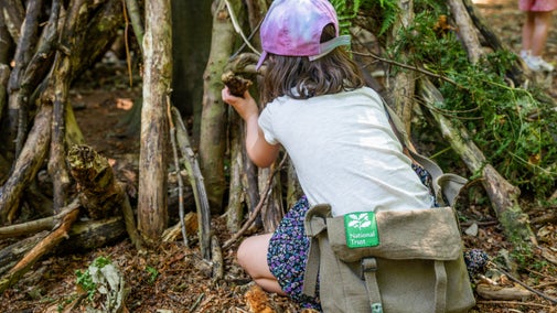 Child in the den building area at Felbrigg Estate wearing tracker pack bag, which is free to borrow.